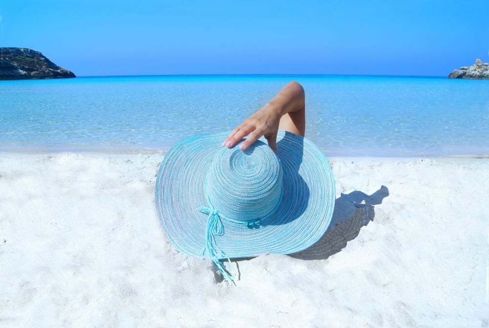 Prevention from sun damage being depicted by wearing a large brimmed hat whilst on the beach in the sun.